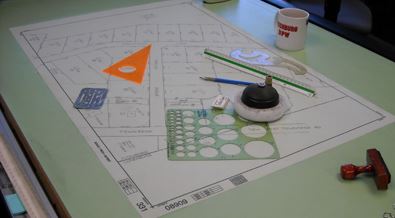 A drafting table with multiple drafting tools sprawled over plans